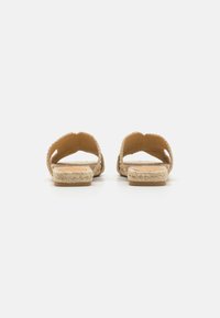 Flate sandaler laget av vevd naturfiber med avrundede åpne tær og en teksturert stropp. Lys beige farge, minimalistisk design.