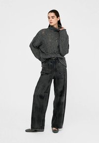 Suéter gris de punto con cuello vuelto y patrón texturizado, combinado con pantalones negros de pierna ancha con efecto cepillado y brillo sutil.