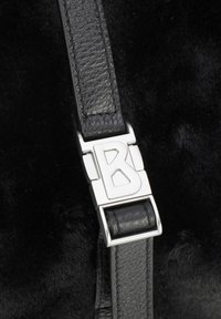 Bracelet en cuir texturé noir avec boucle en métal argenté portant la lettre "B" gravée, sur fond de fourrure noire.