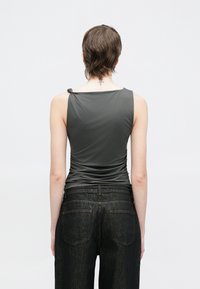 Haut sans manches gris avec un design froncé à l'arrière et un détail noué sur l'épaule, porté avec un jean en denim foncé avec poches arrière.