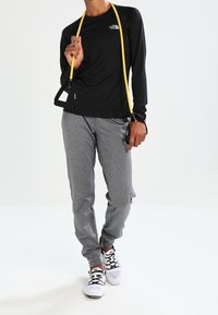 Czarna sportowa koszulka z długim rękawem z logo The North Face, szare zwężane spodnie dresowe i czarno-białe tenisówki. Żółta taśma oporowa w ręce.