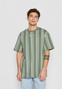 Grönrandig t-shirt med korta ärmar, med vita vertikala ränder och en liten logotyp på bröstet. Mjuk bomullsmaterial.