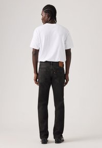 Μαύρα τζιν από τζιν ύφασμα με πέντε τσέπες και σχεδίαση με ίσια γραμμή, σε συνδυασμό με απλό λευκό μπλουζάκι, εμφανιζόμενα από την πίσω πλευρά.