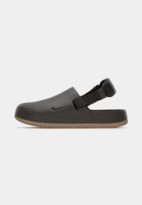 Crne slip-on cipele s gumenim potplatom, s jednostavnim dizajnom i podesivom stražnjom trakom. Nike logo urezan sa strane.