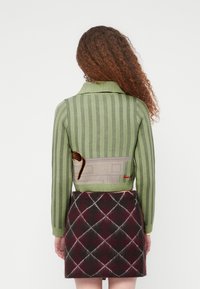 Άτομο με σγουρά μαλλιά που φοράει ένα πράσινο ριγέ κοντό πουλόβερ και μια σκούρα κόκκινη και μαύρη καρό φούστα, βλέποντας από πίσω.