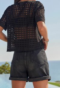 Černý háčkovaný top s diamantovým vzorem, krátké rukávy, spárovaný s tmavými denimovými šortkami s vysokým pasem a ohrnutým lemem.