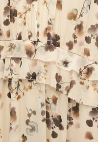 Tissu beige transparent avec volants superposés présentant un motif floral en marron clair, blanc et tons pastel atténués.