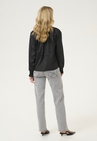 Blusa nera a maniche lunghe con design floreale testurizzato, abbinata a jeans dritti grigio chiaro e scarpe con tacco aperte nere.