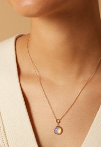 Gouden halsketting met een ronde hanger met een lavendel- en gele edelsteen. Fijne ketting met een delicate textuur, rustend op het sleutelbeen.