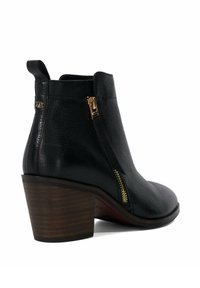 Bottines noires en cuir texturé, avec une fermeture éclair dorée sur le côté, un bout arrondi et un talon en bois moyen avec des rayures horizontales.