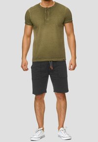 Haut henley à manches courtes vert olive avec trois boutons, associé à un short gris foncé avec des poches et un cordon de serrage. Baskets blanches.