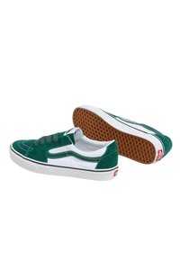 Zapatillas de ante verde con detalles en blanco, punta redonda y ribetes negros. La suela de goma presenta una textura en panal. Diseño con cordones y cintas planas.