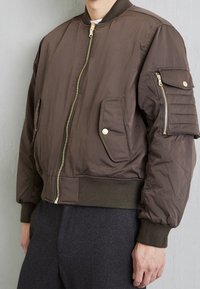 Brown bomber jacket featuring a zip closure, ribbed cuffs and hem, multiple pockets, and a textured fabric finish.