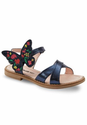 Navy blue sandals with a shiny finish, featuring a floral embroidered butterfly accent and crisscross straps over a light-colored sole.