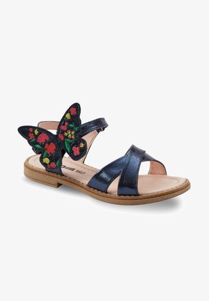 Mornarji modre sandale s sijočim zaključkom, ki imajo cvetlični vezen metulj kot poudarek in čez svetlo barvno podplat so križno spletene naramnice.