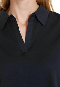 Námořnická modrá blůza s límečkem a výstřihem do V, vyrobená z hladké látky s jemným leskem v oblasti límce. Žádné viditelné vzory ani kování.