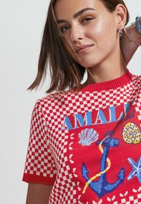 Suéter de punto a cuadros rojos con gráficos de ancla azul y conchas marinas con detalles multicolores. Cuello acanalado y mangas cortas.