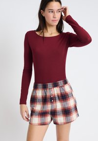 Top burdeos de manga larga combinado con pantalones cortos de cuadros en crema, azul marino y rojo, con una cinturilla elástica y botones decorativos.