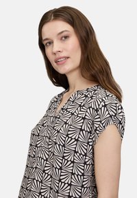 Zwart en crèmekleurig gebloemd blouse met een v-hals, korte kapmouwen en een geometrisch bladpatroon. Soepele stofstructuur.