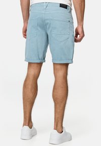 Lichtblauwe denim shorts met omgeslagen pijpen, voorzien van twee achterzakken en een zwart merklabel op de tailleband. Draag ze met witte sneakers.