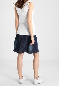 Falda de mezclilla con forma acampanada, color azul oscuro y acentos de lavado claro. Combinada con una camiseta sin mangas blanca ajustada y zapatillas blancas.