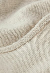 Kremowa dzianina o miękkiej fakturze. Charakteryzuje się gładką, skręconą krawędzią oraz widocznym wzorem szwów na całej powierzchni.