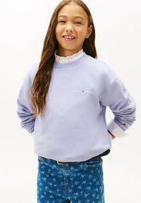 Lyslilla sweatshirt med ribbet halsudskæring, der har et lille logo på brystet. Kombineret med bukser i blå med blomsterprint.