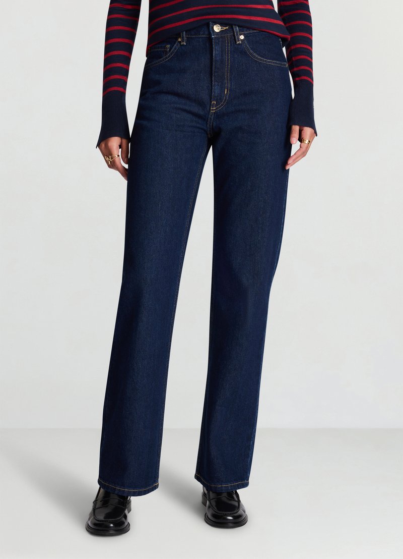 Jean large en denim bleu marine à taille haute, coutures contrastées et accessoires argentés. Associé à un haut à manches longues rayé bleu marine et rouge.