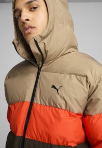 Dugnas striukė su rausvu viršumi, oranžine vidurine dalimi ir tamsiai žalia apatine dalimi. Yra užtrauktukas ir juodas Puma logotipas. Tekstūruota medžiaga.