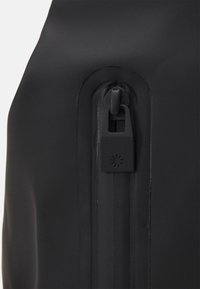 Angolo di una borsa nera impermeabile con una chiusura lampo sicura, dotata di un cursore sagomato e una superficie liscia e opaca.