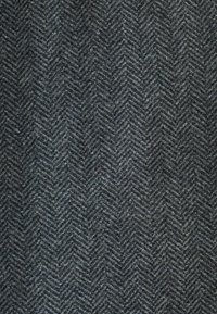 Tessuto herringbone scuro con una trama testurizzata, caratterizzato da diverse tonalità di grigio e delicate sfumature, che presenta un aspetto durevole e strutturato.