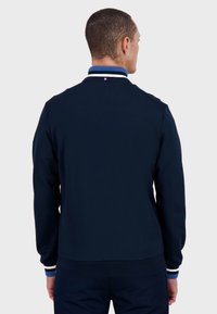 Felpa blu navy con colletto a costine caratterizzato da strisce bianche e blu. Texture liscia, design aderente e cuciture sulle spalle in evidenza.