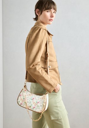 Kamelijas krāsas mākslīgā zamšā jaka ar rāvējslēdzēju, kombinēta ar piparmētru zaļām cargo biksēm. Tur rokās baltu ziedu raksta somiņu ar zelta ķēdes siksnu.