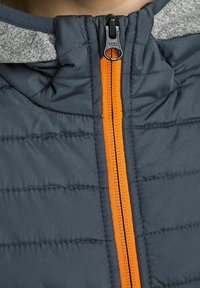 Padded jacket w ciemnoniebieskiej korpusie i szarej kapture, z pomarańczowym zamkiem błyskawicznym i pikowanym wykończeniem dla dodatkowej izolacji.