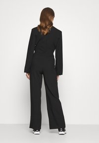 Mono negro con mangas largas y pantalones anchos, confeccionado en una tela suave. Los detalles notables incluyen un diseño estructurado y costuras mínimas.