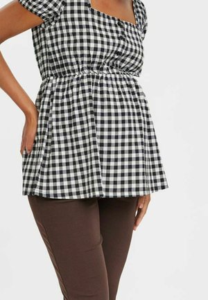 Zwart-witte geruite peplum top met een vierkante halslijn en korte mouwen, gecombineerd met strakke bruine broek. Knopdetails aan de voorkant.