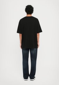 Black cotton t-shirt with a relaxed fit, short sleeves, and a straight hem, paired with dark blue jeans and sneakers.