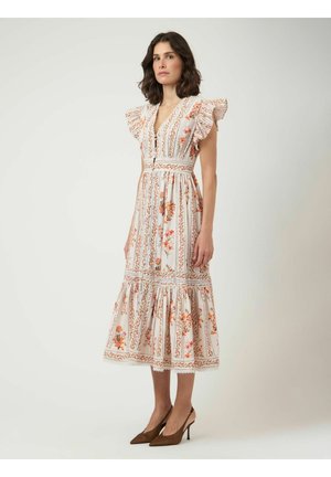 Kvinne iført en hvit midi-kjole med oransje blomstertrykk, rynkede ermer, V-hals og brune spisse pumps.