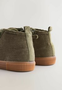 Bottes ankle en velours côtelé vert avec une surface texturée, un talon renforcé et une semelle extérieure en caoutchouc gomme dotée de stries verticales pour l'adhérence.