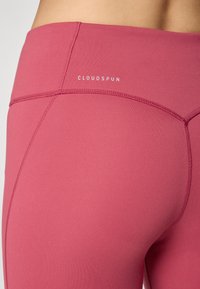 Ružičaste atletske tajice sa dizajnom koji se tijesno prilagođava tijelu. Napravljene od glatkog materijala, s ravnim šavovima i malim logotipom "CLOUDSPUN" blizu pojasa.
