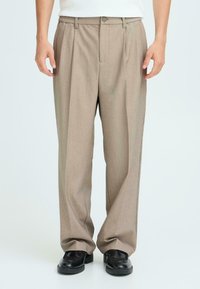 Beige geplooide broeken van textiel, voorzien van een knoopsluiting, zijzakken en een relaxte pasvorm, gestyled met zwarte schoenen.