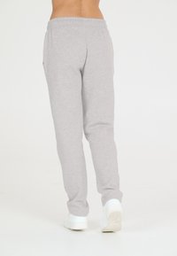 Grå bomullsträningsbyxor med elastisk midja, sidofickor och avsmalnande ben, tillsammans med vita sneakers på en neutral bakgrund.