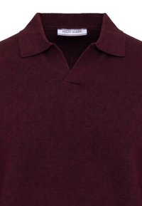 Polo en maille bordeaux foncé avec un col doux et une petite étiquette blanche à l'intérieur de l'encolure portant la mention Felix Hardy.