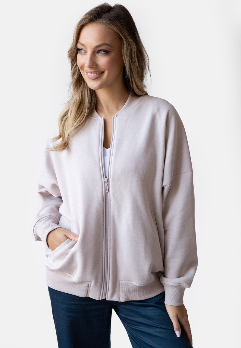 Jasnopurpurowa kurtka zapinana na zamek, wykonana z miękkiego materiału, z ściągaczami przy mankietach i kieszeniami bocznymi; luźny fason i prosty design bez dodatkowych wzorów.