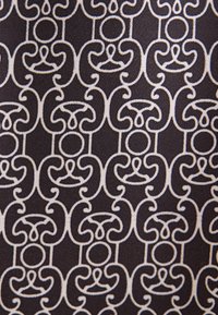 Tissu foncé avec des motifs géométriques blancs brodés de façon répétitive, composés de cercles et de lignes courbes dans un design symétrique et interconnecté.