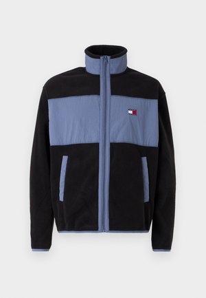 Fleece jacket with high collar, featuring a black body and light blue upper sections, zip closure, and two side pockets.