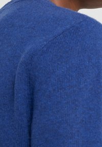 Niebieski sweter dziany o fakturowanym wykończeniu, z zaokrąglonym dekoltem i widocznymi szwami. Zbliżenie podkreśla miękką jakość tkaniny.