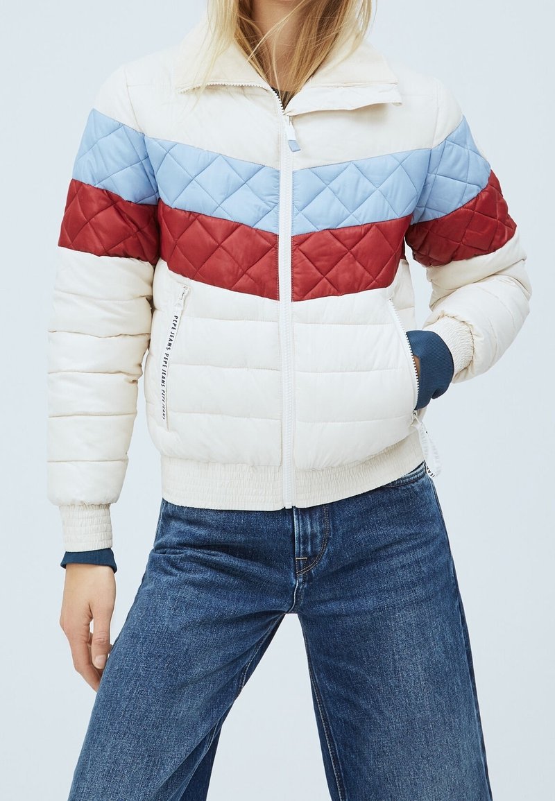 Prošívaná péřová bunda s barevnými bloky v krémové, modré a červené barvě, se zipem a žebrovanými manžetami. Švy dodávají texturu.