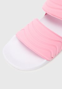 Ροζ σανδάλι με φάσες με κυματιστή υφή, λευκή σόλα και απαλό, ματ φινίρισμα. Διακοσμημένο με ραμμένα σχέδια.