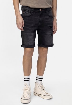Denim shorts in dark wash with a distressed effect, rolled cuffs, and five pockets. Worn with white crew socks and beige high-top sneakers.